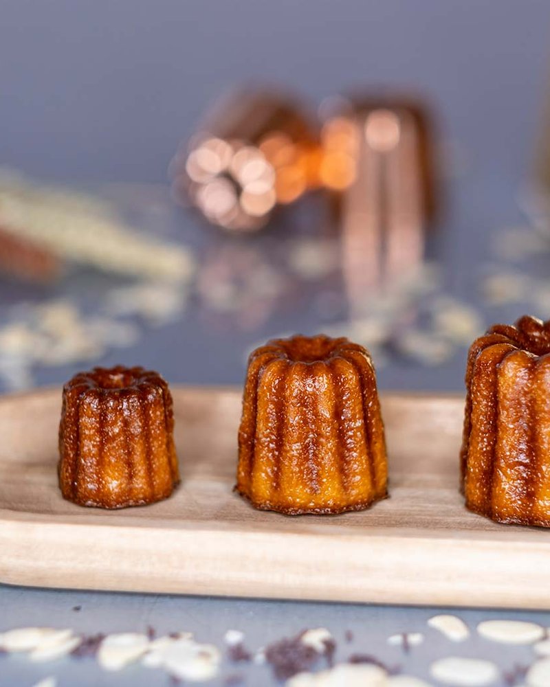 Trois cannelés de Bordeaux de tailles différentes, sur un plateau en bois, La Toque Cuivrée